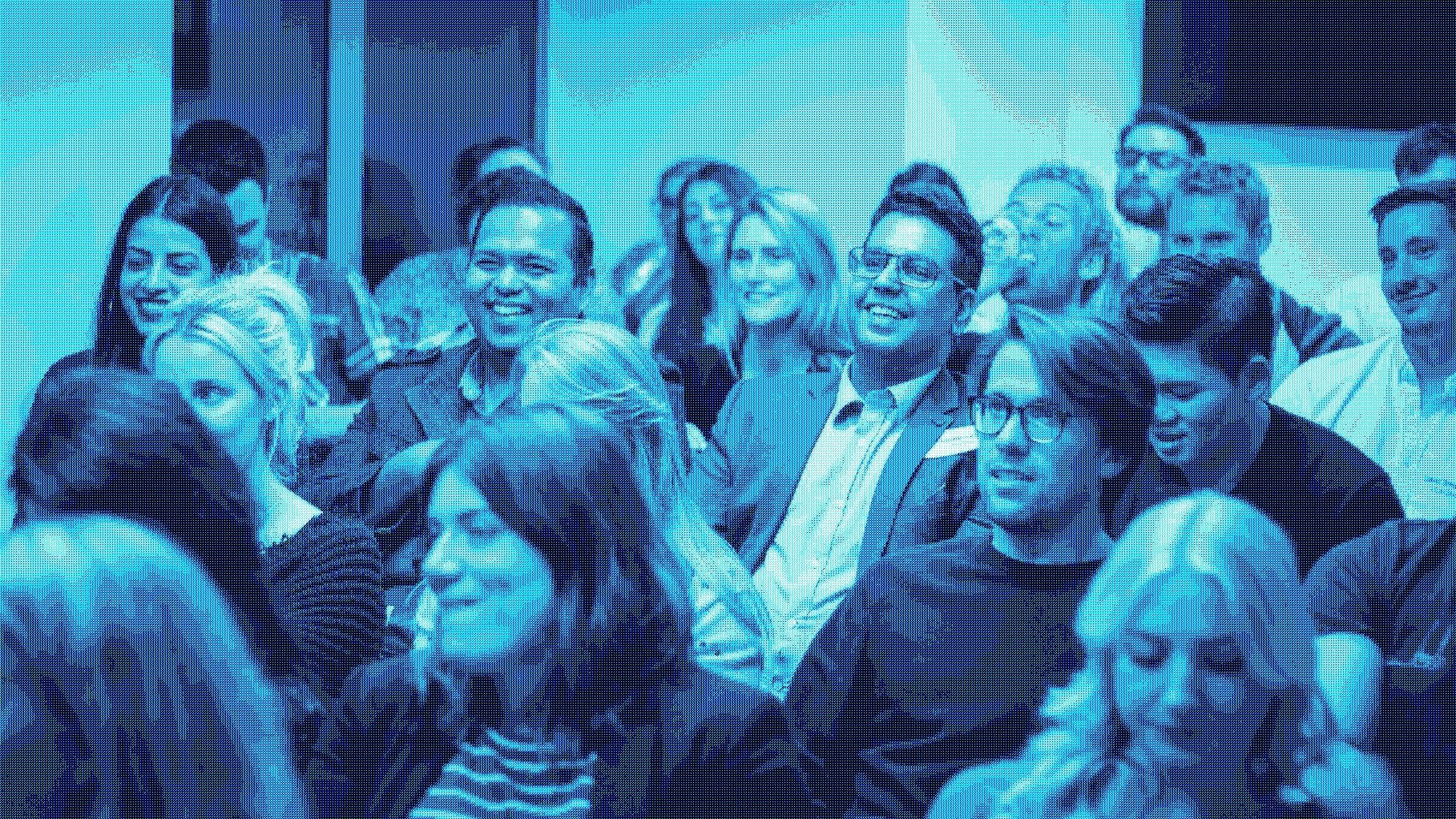 A diverse group of people at a conference, blue tint, via Wes Lewis / Unsplash